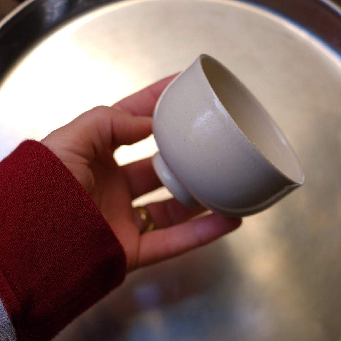 Hand holding a white ceramic bowl in front of a metallic surface