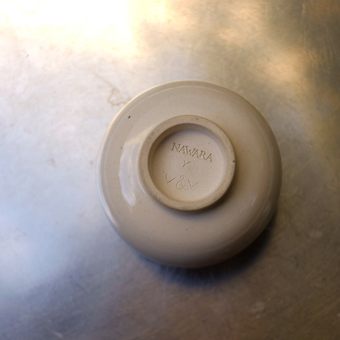 Ceramic cup with 'Nawara x v&v' branding on a metallic surface