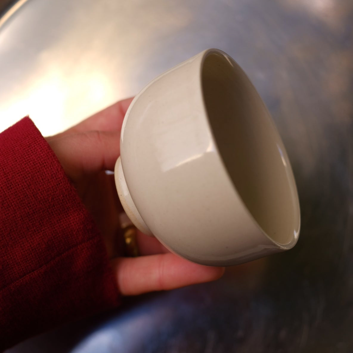 Person holding a small white cup in front of a large metallic pot